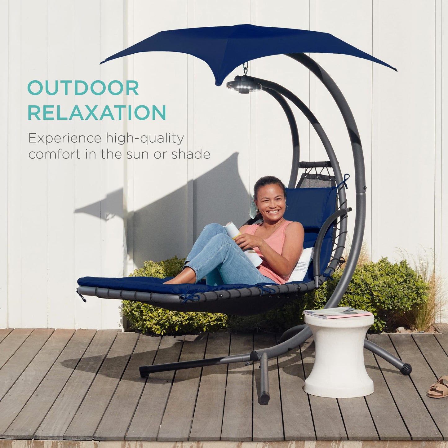 Hanging curved steel chaise lounge swing with canopy and pillow, navy blue.